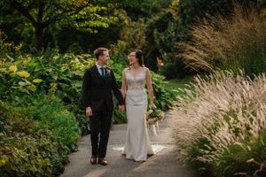 Couple walking together on garden path surrounded by lush ornamental grasses and greenery.