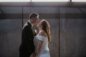 A romantic couple embraces in a dimly lit industrial space with concrete walls and dramatic shadows.