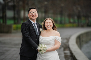 A happy couple in wedding attire smile together on a curved path in an outdoor setting.
