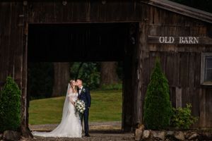 A romantic wedding photo taken under an old barn entrance with rustic wooden details.