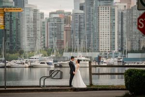 A couple in wedding attire embraces near a yacht marina with a modern city skyline in the background.