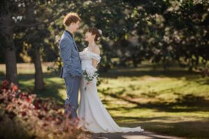 Couple shares tender moment in sunlit park with blooming cherry blossoms and trees.
