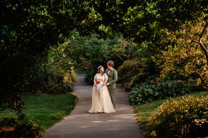 A scenic outdoor wedding portrait with couples walking through park pathways in golden sunlight during autumn.