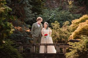 A happy couple in light-colored formal attire shares loving moments on a bridge in a lush Japanese garden setting.