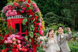A red British phone booth decorated with pink and red roses creates a romantic garden wedding photo backdrop.