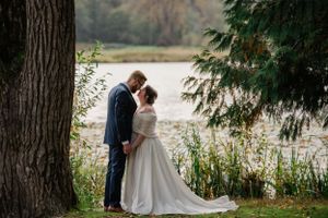 A romantic moment between two people by a lake with evergreen trees in the background.