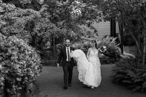 A couple walks along a garden path surrounded by lush greenery in black and white.