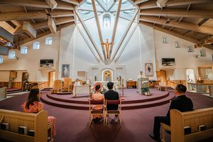 Small wedding ceremony inside a modern Catholic church with wooden architecture and skylight above the altar.