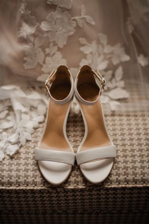 Elegant white wedding sandals with ankle straps displayed on a textured surface.