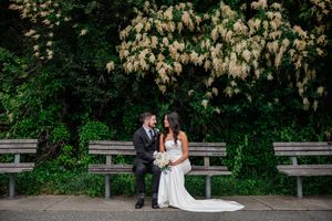 A couple sits on a wooden bench under blooming white yucca flowers in a lush garden setting.