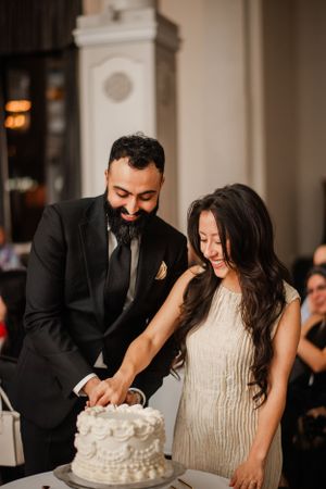 Newlyweds share a joyful moment while cutting their white wedding cake.