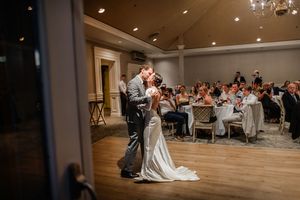 A couple dances intimately together during their first dance at a wedding reception with guests watching from tables.