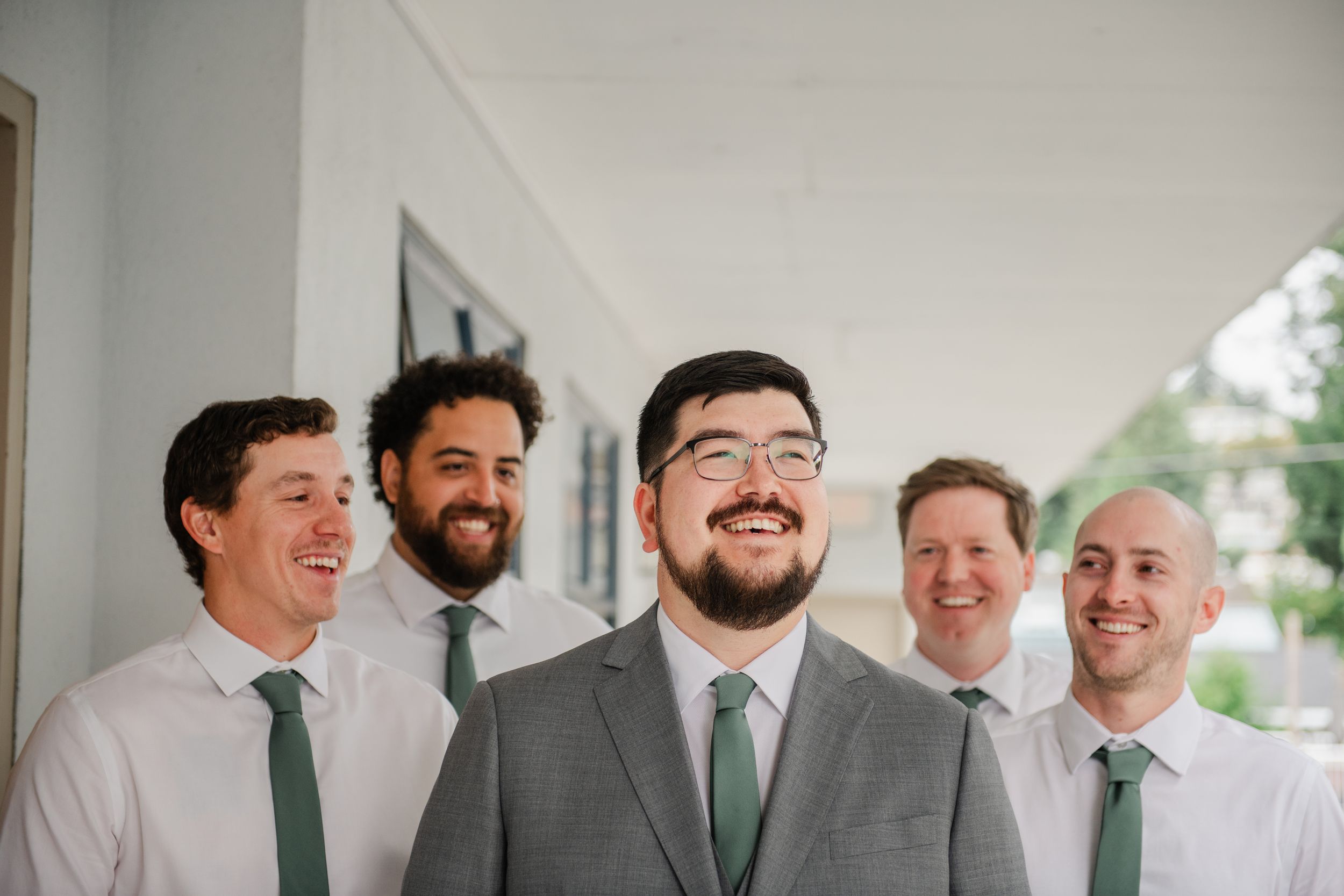 Groom in gray suit with green tie smiles with four groomsmen in white shirts and green ties at wedding.