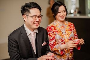 Couple in traditional Chinese wedding attire share a joyful moment during tea ceremony.