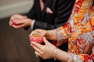 Close up of hands holding traditional red Chinese teacups during wedding tea ceremony.