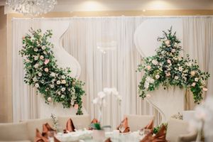 Elegant wedding reception backdrop with white draping and lush floral arrangements of pink roses and greenery.