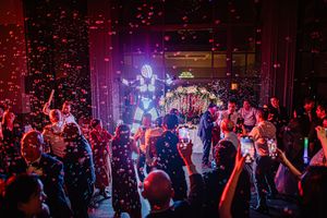A crowded nightclub dance floor filled with people dancing under colorful purple and red lighting effects.