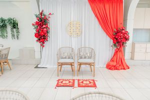 Chinese wedding ceremony setup with red floral arrangements, draped fabric, two rattan chairs, and traditional red kneeling mats.