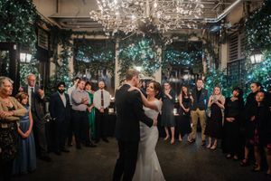 A couple shares their first dance at an elegant indoor wedding reception under a crystal chandelier with greenery decor.