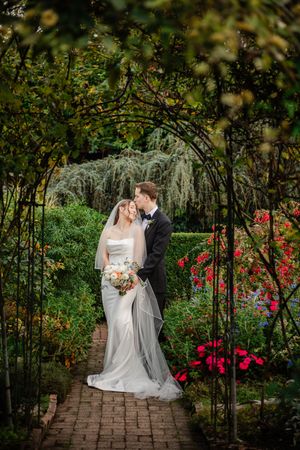 Romantic garden wedding photos captured in sequence along a brick path surrounded by blooming red roses and greenery.