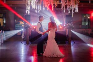A couple dances under hanging lights with dramatic red lighting in an indoor venue.
