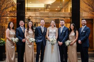 Wedding party in formal attire posing outside modern building at dusk.