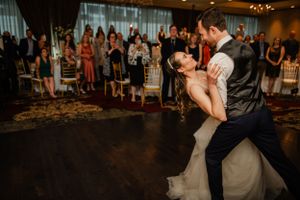 A couple performs a dramatic dip during their first dance on a dark ballroom floor.
