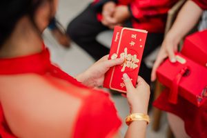 Woman in red dress holding a red Chinese lucky money envelope with gold decorations during a traditional celebration.