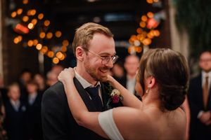 A couple shares an intimate moment during their first dance at a wedding reception with warm bokeh lights in background.