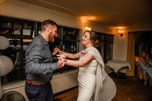 A couple in wedding attire share an intimate dance together in a warmly lit indoor venue during their reception.