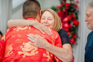 Woman smiling warmly while hugging a man in a red dragon print shirt at a wedding ceremony.