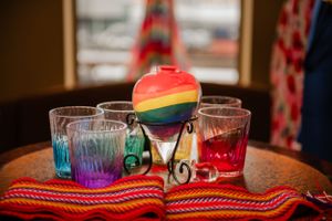 Rainbow colored glasses and decorations arranged on a colorful striped cloth.