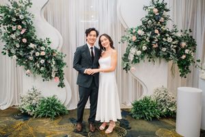 Couple posing together at elegant wedding venue with floral backdrop featuring pink roses and greenery.