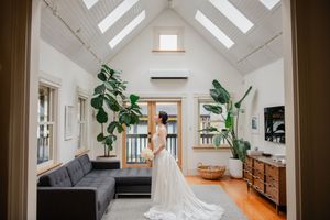 Elegant bridal gown displayed in a modern living room with skylights, indoor plants, and gray sofa.