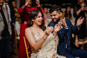 A couple laughs together during a celebratory moment at their wedding reception with guests in the background.
