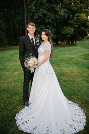 Newlyweds share an intimate moment outdoors on a lush green lawn with a beautiful white lace wedding dress train.