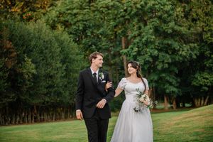 Wedding couple walks together through vibrant green garden path during summer outdoor celebration.