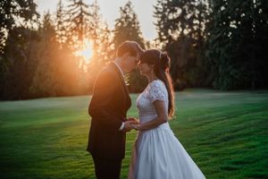 Silhouetted couple embraces on a grassy field during golden hour sunset with evergreen trees in background.