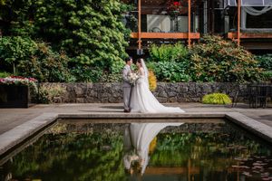A couple's reflection mirrors in a tranquil pond beside a stone wall and verdant garden setting.