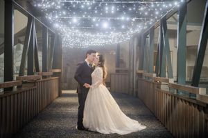 A couple shares a romantic moment on a covered bridge illuminated by twinkling string lights overhead.