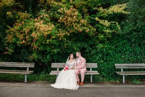 Bride and groom sitting on a bench surrounded by lush green trees on their wedding day.
