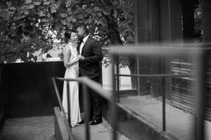 Black and white photograph of a couple embracing in an urban setting with architectural elements visible.