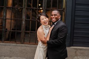 Newlywed couple sharing laughter and embraces outside a rustic industrial building.