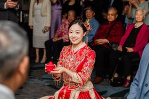 Traditional Chinese tea ceremony with person in red qipao dress serving tea to seated guests during wedding celebration.