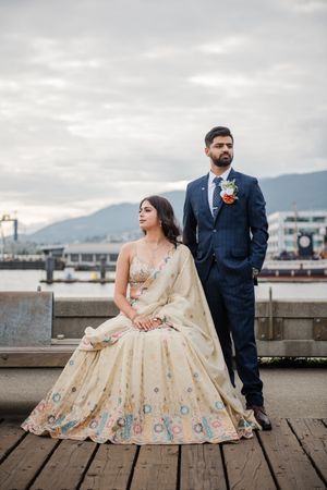 Couple shares joyful moments on a wooden pier with mountains and city skyline in the background, bride wearing ornate gown.
