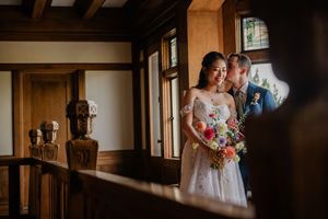A wedding couple stands in a sunlit hallway with wooden walls and warm lighting creating a romantic atmosphere.