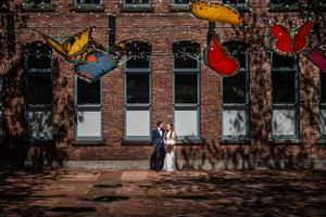 Couple stands against brick wall with colorful butterfly decorations.