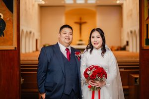 Wedding ceremony inside a church with couple standing at altar and red roses bouquet in focus.