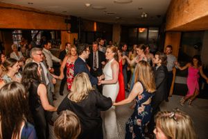 Wedding reception guests dance and celebrate on a crowded dance floor in a rustic venue.