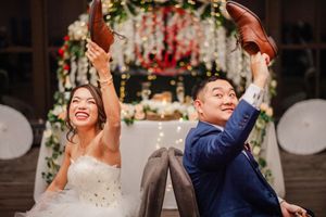 A joyful couple celebrates during their wedding reception as guests cheer and clap in a beautifully decorated venue.